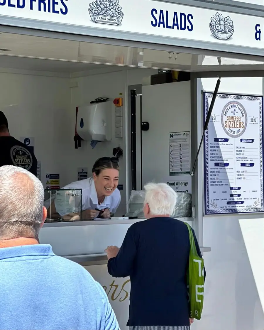 A smiling member of the team taking an order at the hatch, with the menu board beside her