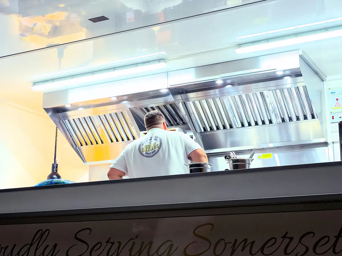 Inside the trailer: a chef in a Somerset Sizzlers T-shirt working under the stainless-steel extraction canopy
