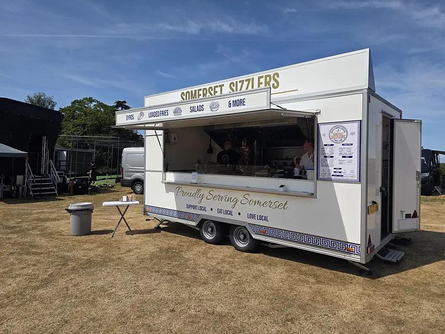 The Somerset Sizzlers trailer set up and serving at an outdoor event, hatch open with the menu board on display
