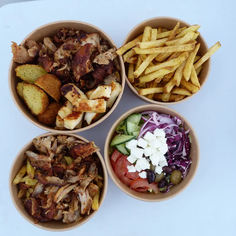 Four Somerset Sizzlers boxes from above: gyros with halloumi and falafel, seasoned fries, chicken gyros on fries and a Greek salad with feta