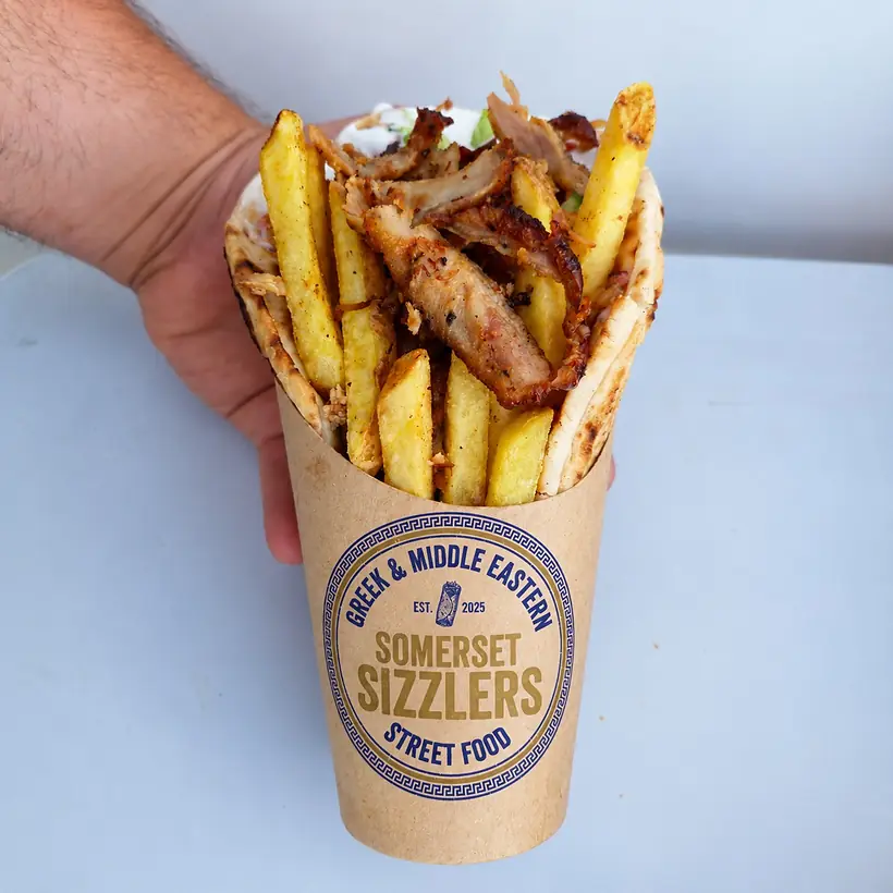A Somerset Sizzlers chicken gyros wrap — warm pitta packed with gyros, chips, salad and tzatziki — held up in a branded cup